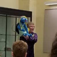 A woman holds up a blue puppet with yellow hair